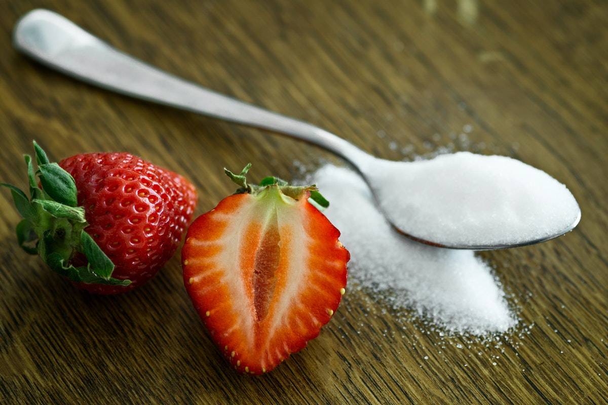 A strawberry cut in half next to a spoon full of allulose sweetener.