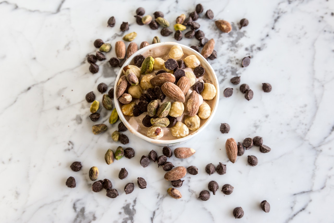 Dark chocolate chips in bowl with almonds and other types of nuts.