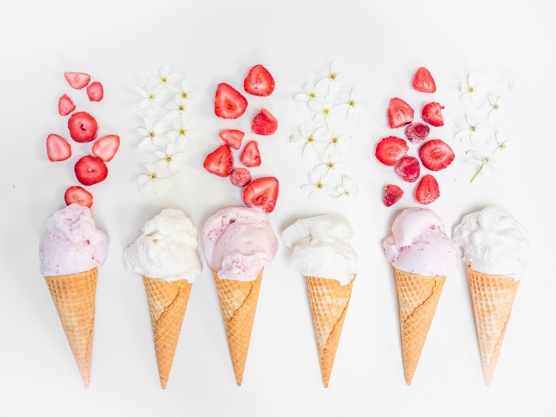 6 ice scoops on cones surrounded by strawberries and vanilla