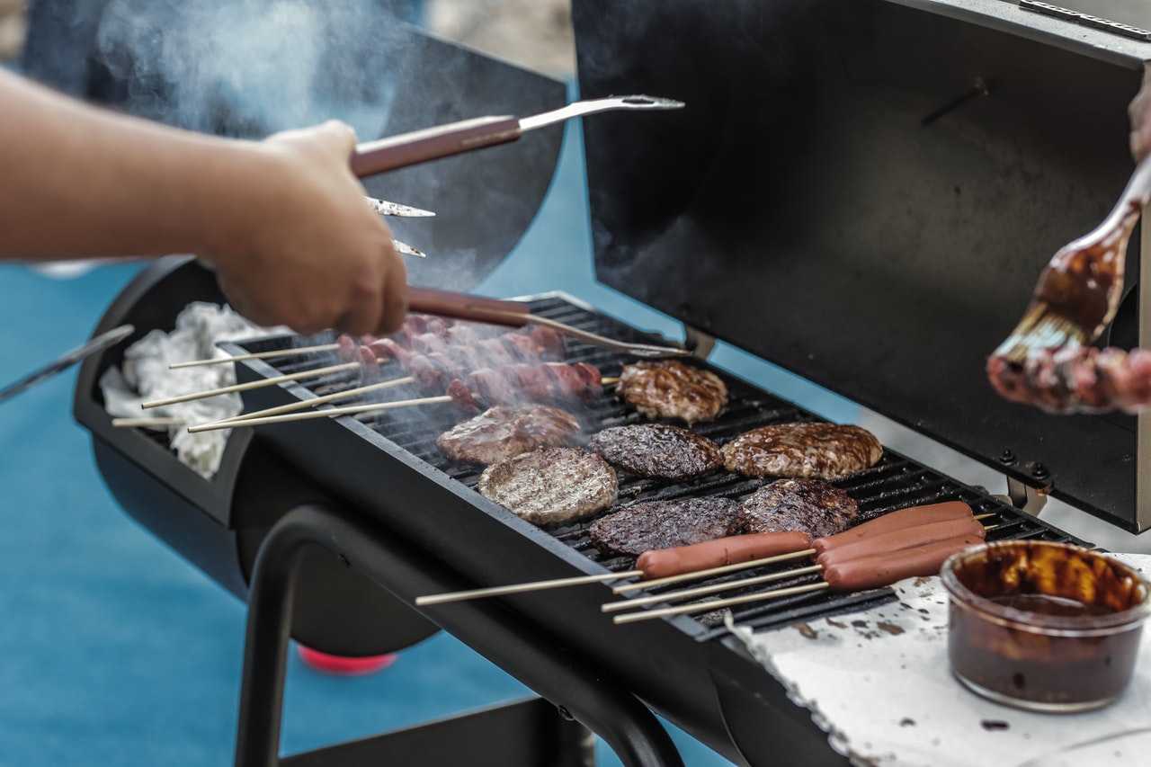 Man flipping burgers and hot dogs on outdoor grill for summer party.